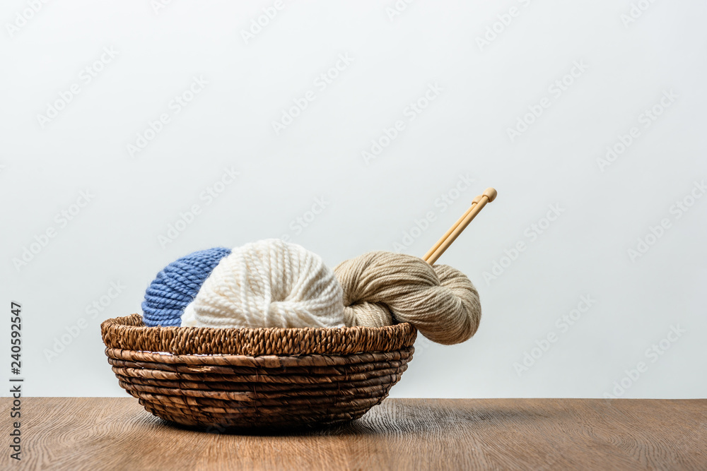 close up view of yarn with knitting needles in wicker basket on wooden tabletop on grey background close up view of yarn with knitting needles in wicker basket on wooden tabletop on grey background