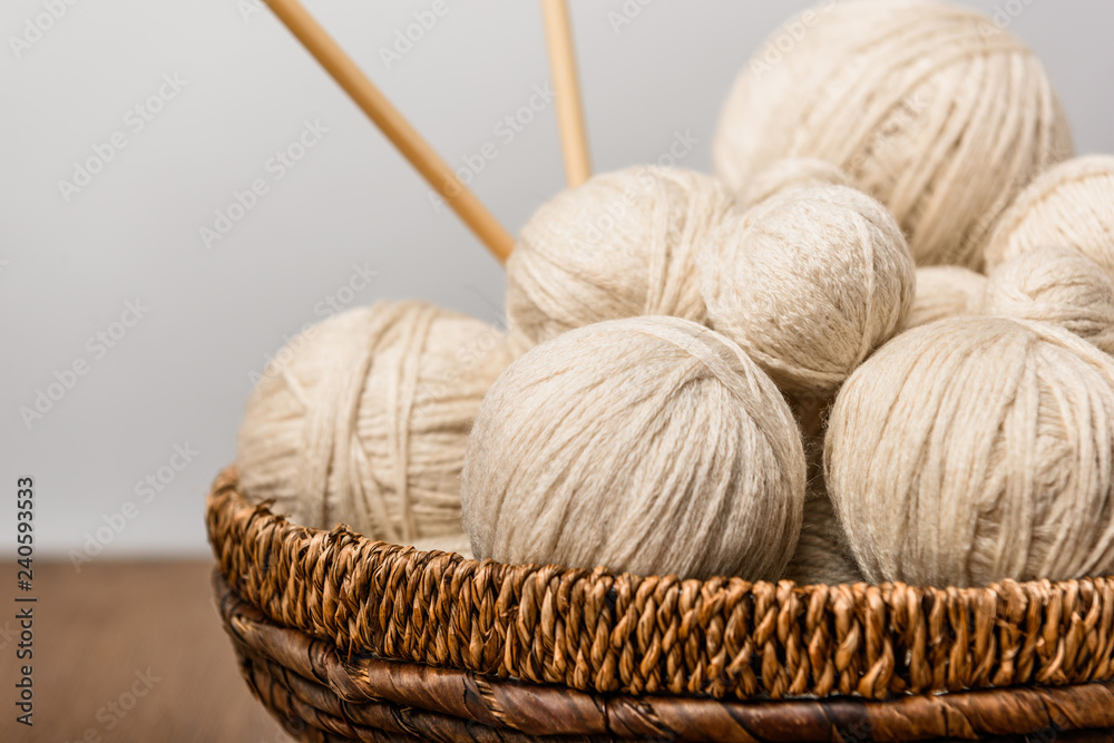 close up view of yarn clews and knitting needles in wicker basket on grey background close up view of yarn clews and knitting needles in wicker basket on grey background