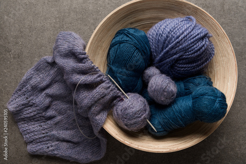 flat lay with purple and blue yarn balls in bowl on grey background