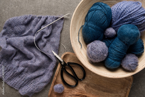 flat lay with purple and blue yarn balls with scissors and knitting needles on grey background