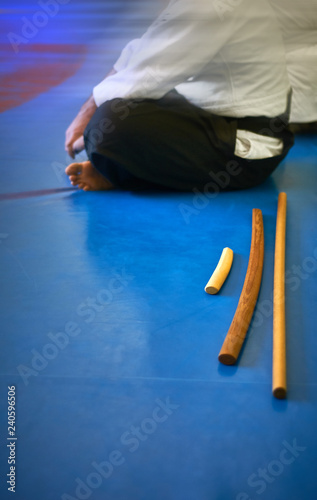 Aikido background. Tanto, bokken and jo on a blue wrestling mat. The background is a man in white kimano and black hakama. Web banner with with blurred background, place for text. Without faces.