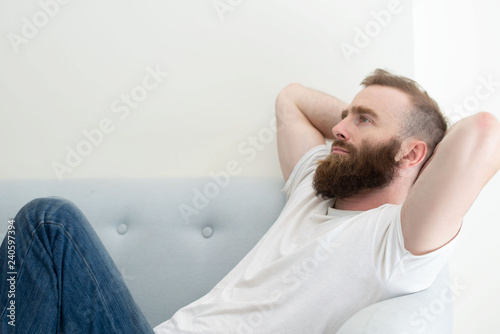 Sad fired employee depressed about job loss. Bearded young man in casual resting on couch at home and staring into vacancy. Unemployment or depression concept © Mangostar