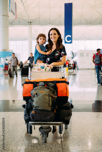 Mother holding a baby girl at the airport and pushing a trolley with the luggage