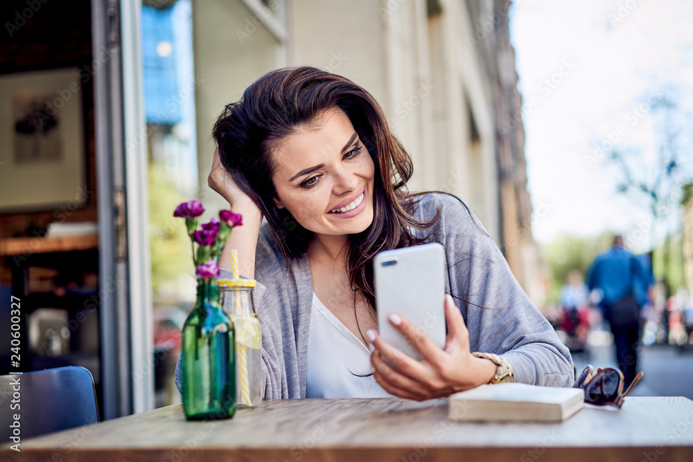 Happy woman looking at cell phone at outdoors cafe