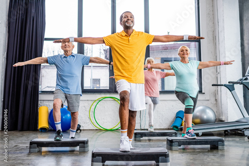 smiling senior multicultural athletes synchronous exercising on step platforms at gym