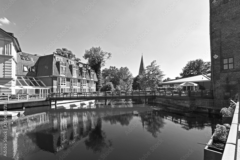 Black and white photo of the river Ilmenau in the German medieval town of Lueneburg. You can see from left to right a cafe, the tower of 