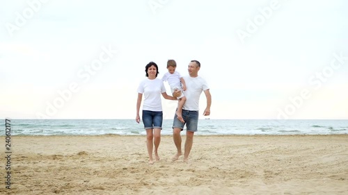 A happy family walks along the sandy beach on a sunny day. Recreation and tourism. People move towards the camera, leaving the focus. photo