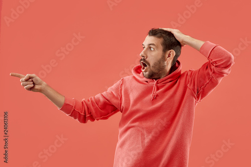 Wow. Attractive male half-length front portrait on coral studio backgroud. Young emotional surprised bearded man standing with open mouth. Human emotions, facial expression concept. Trendy colors