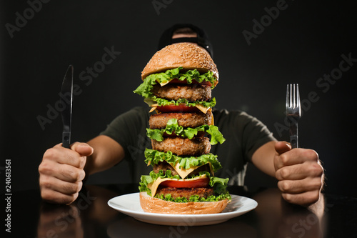 Man with cutlery eating huge burger on black background