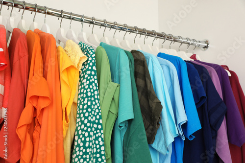 Hangers with different colorful clothes on rack in wardrobe