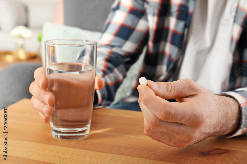 Man holding pill and glass of water at table, closeup