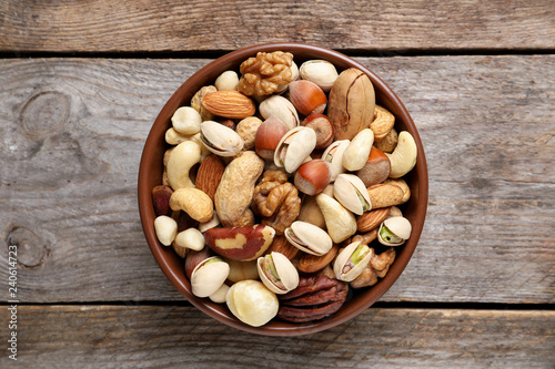 Bowl with mixed organic nuts on wooden background, top view