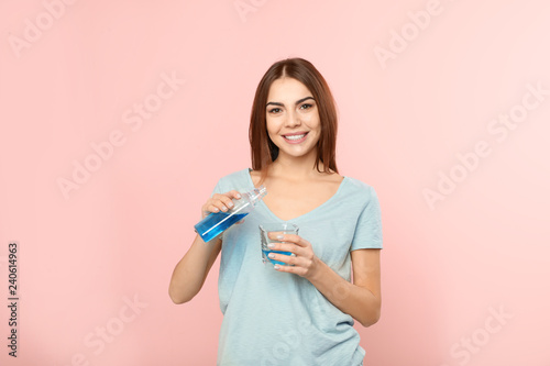 Beautiful woman pouring mouthwash from bottle into glass on color background. Teeth and oral care