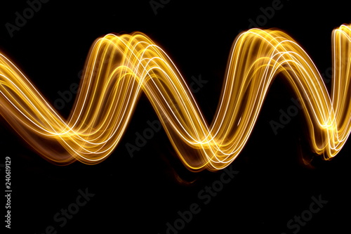 Gold light painting photography, long exposure photo of gold fairy lights in a swirling, wavy pattern against a black background