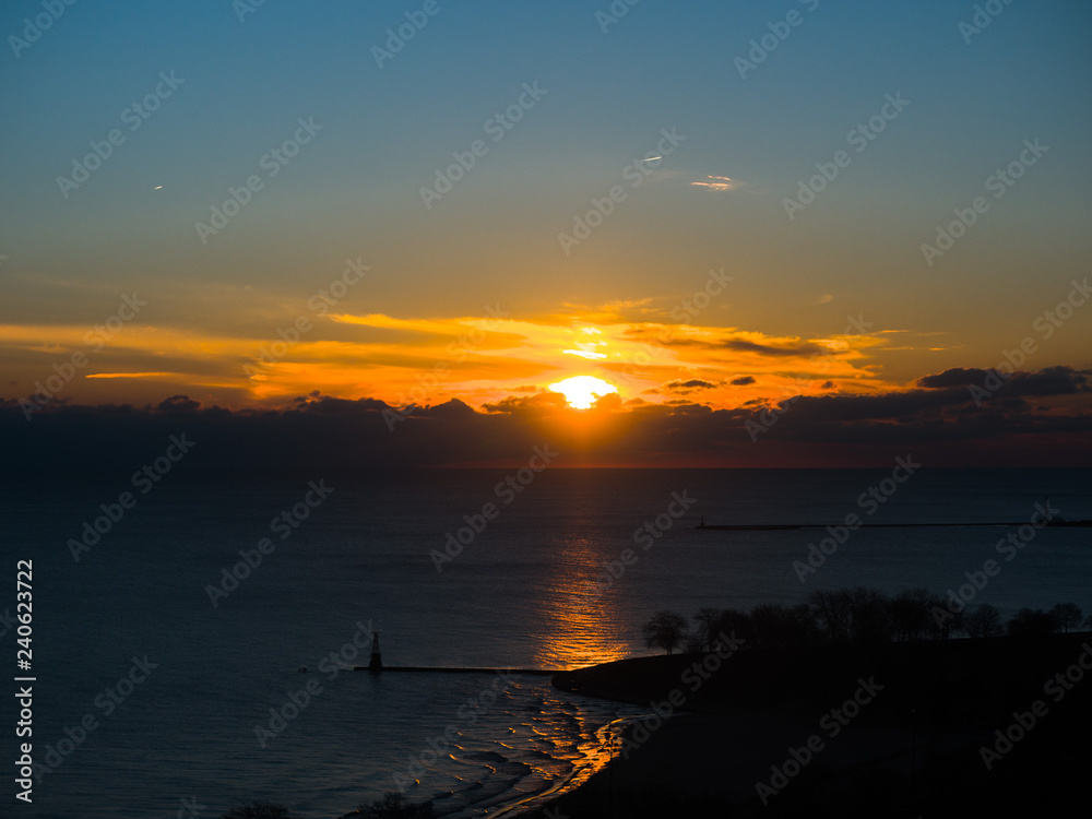 Naklejka premium Beautiful landscape aerial photograph of colorful yellow sunrise over cumulus clouds in Chicago reflecting on the water of Lake Michigan with a pier at Foster Beach sticking out into the water below.