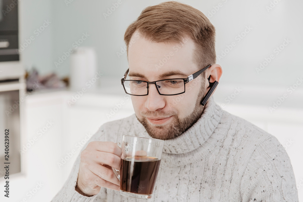 A man with glasses and a beard drinking coffee and working at the computer