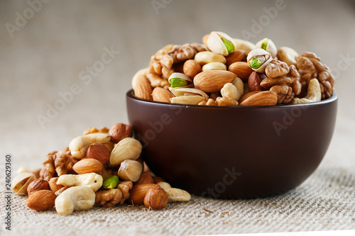 Mix of different nuts in a wooden cup against the background of fabric from burlap. Nuts as structure and background, macro. Top view. photo