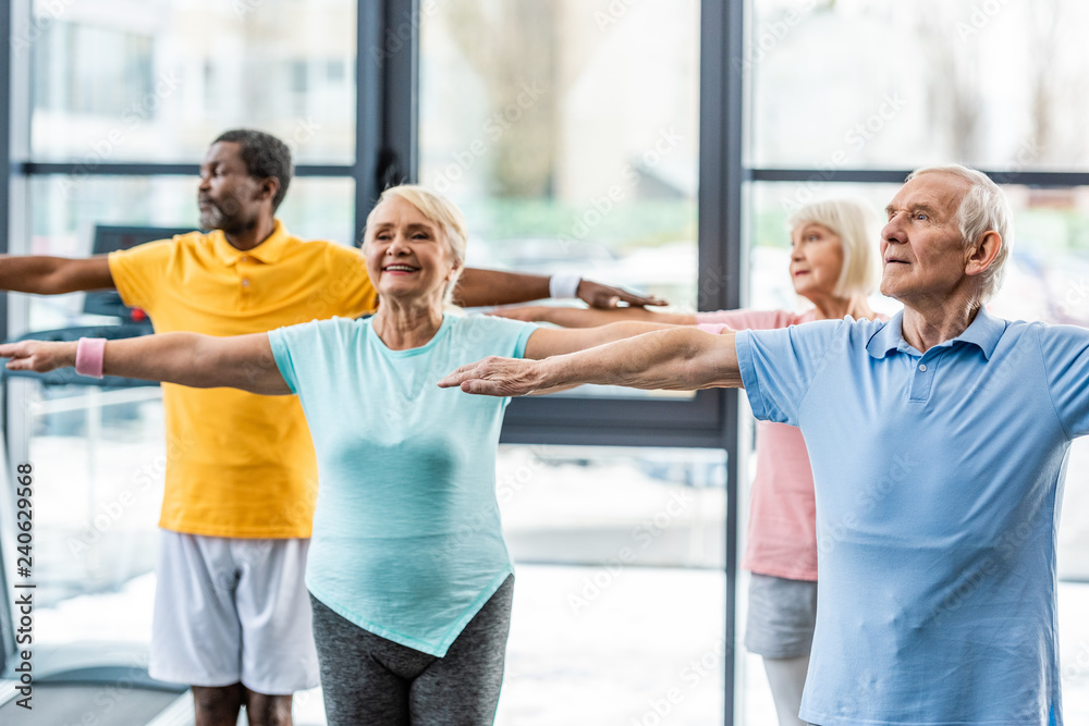 Obraz premium happy multiethnic senior athletes synchronous doing exercise at sports hall