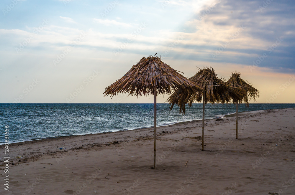 three straw beach umbrellas on an empty seashore on a clear day