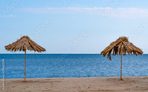 Fototapeta Naklejka Na Ścianę i Meble -  two straw beach umbrellas on an empty seashore on a clear day