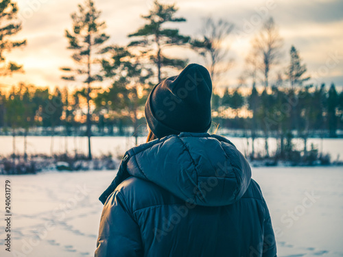Back of girl or woman is watching out in the wild nature in snow winter.