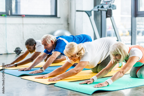 cheerful senior athletes synchronous exercising on fitness mats at gym