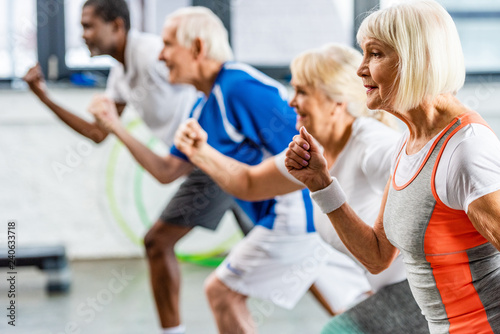 selective focus of senior sportswoman exercising with friends at gym