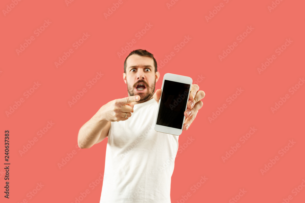 Young handsome man showing smartphone screen over coral background with a surprise face. Human emotions, facial expression concept. Trendy colors Young handsome man showing smartphone screen over coral background with a surprise face. Human emotions, facial expression concept. Trendy colors