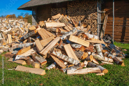 Pile and wall of cut birch wood and stacked wood logs ready for winter, standing on the grass near a Lithuanian typical wooden house