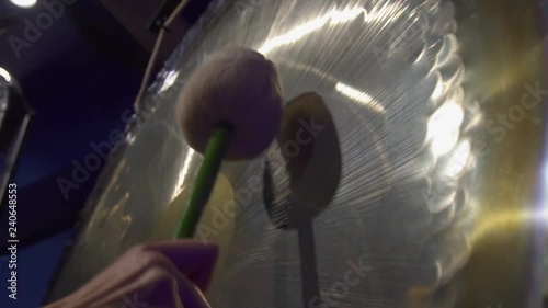 Woman hand hitting a big gong with a special beater in a dark meditation room.