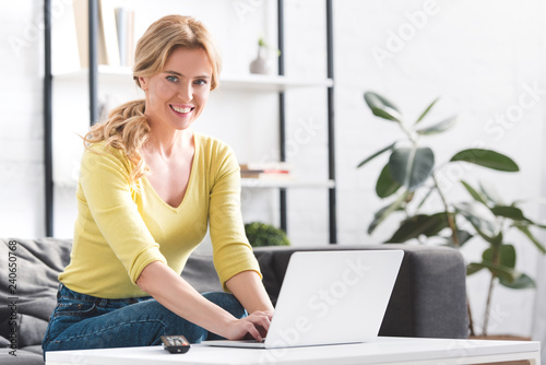 attractive woman using laptop and smiling at camera at home