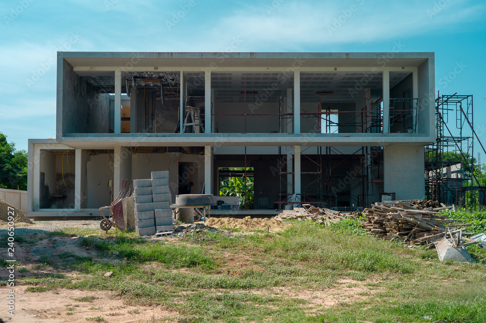 Landscape and perspective of house under construction with piles of materials and equipments with clear blue sky in background Landscape and perspective of house under construction with piles of materials and equipments with clear blue sky in background