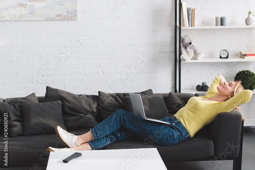side view of happy relaxed woman lying with laptop on couch