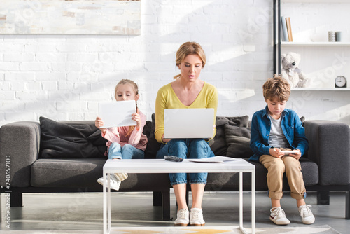 mother and beautiful children sitting on sofa and using digital devices