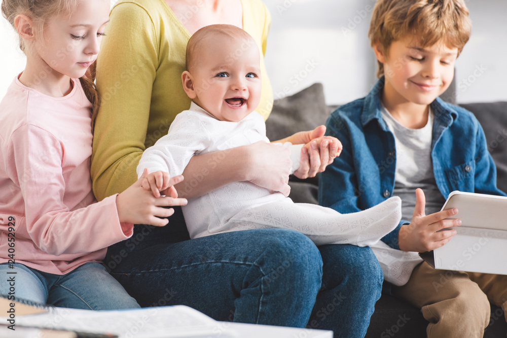 cropped shot of mother with infant child and cute siblings sitting together in sofa cropped shot of mother with infant child and cute siblings sitting together in sofa