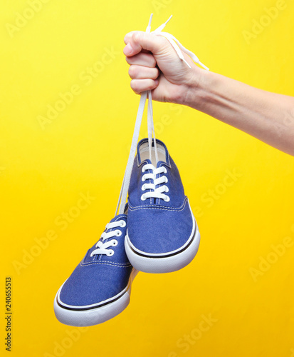The hand holds by shoelaces retro style hipster sneakers on yellow pastel background. Minimalism. © splitov27