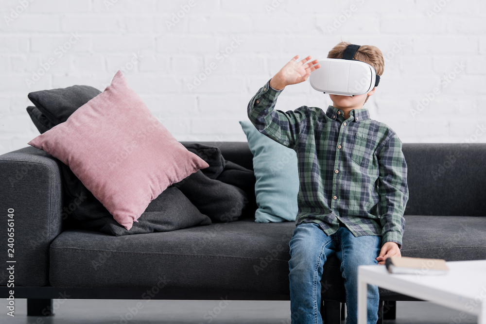 adorable boy sitting on sofa and using virtual reality headset at home