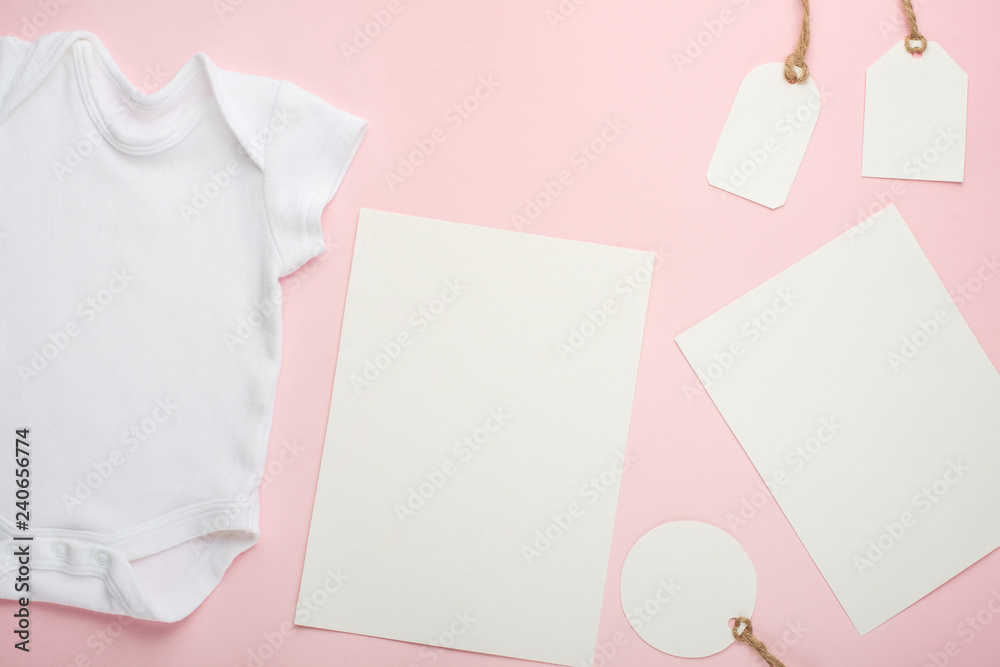 Fototapeta premium Layout Flat Lay white baby bodysuit shirt, on a pink background, for a girl with white postcards and tags.Mock up for design and placement of logos, advertisements