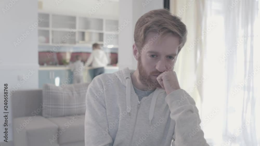 Portrait of sad bearded man standing in living room close up. Woman and boy are in the background. Family relationships. Family problems. Slow motion. Portrait of sad bearded man standing in living room close up. Woman and boy are in the background. Family relationships. Family problems. Slow motion.