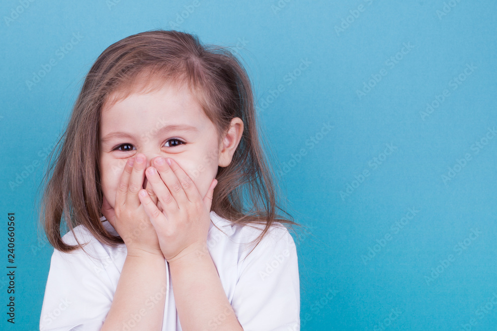 Little girl on a blue background laughs covering her face with her hands Little girl on a blue background laughs covering her face with her hands
