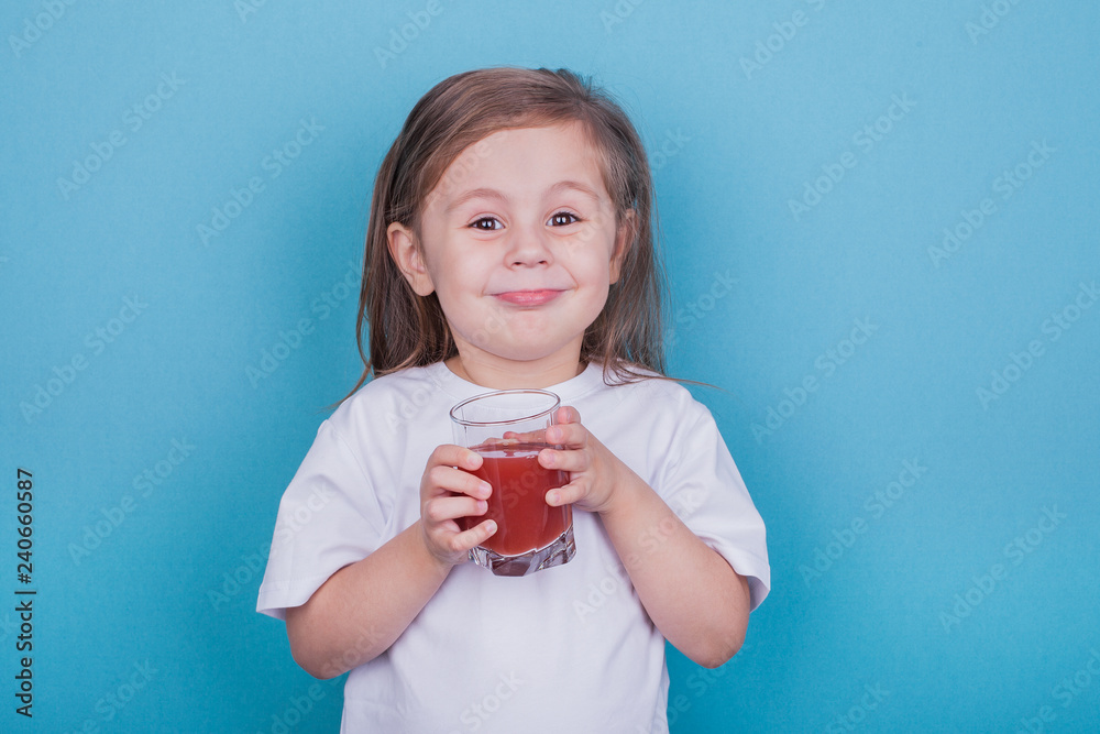 Cute little girl drinking juice from glass on blue background