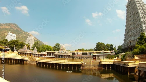 Pond among sculptural towers of southern temple complex Tiruvannamalai holy mountain Arunachala on background reflection in water photo