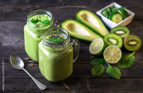 Green smoothie on dark background with avocado, spinach, lemon and kiwi on the right side.