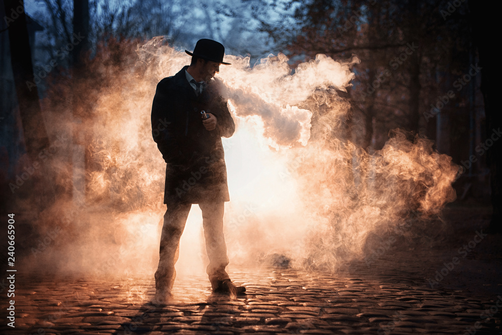Obraz premium Vaping man in black hat holding a mod. A cloud of vapor.
