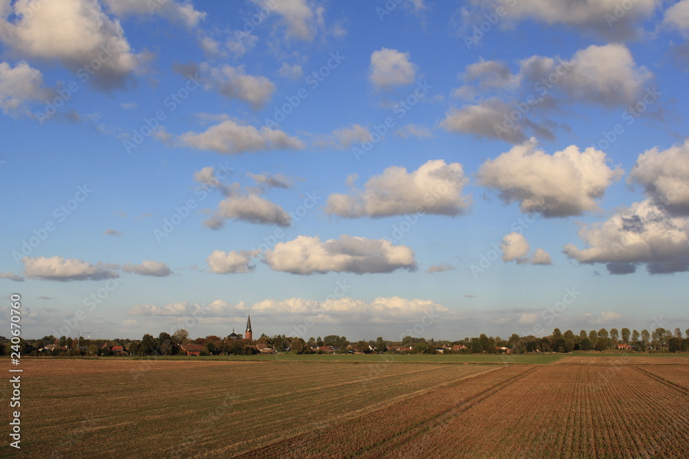 a little village in the dutch countryside with ploughed land in front and a blue sky with white clouds in the background