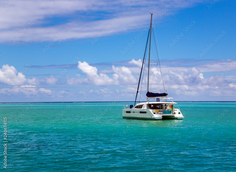 Lonely catamaran in a beautiful turquoise lagoon near the island Bora Bora in the Leeward group of the Society Islands of French Polynesia.