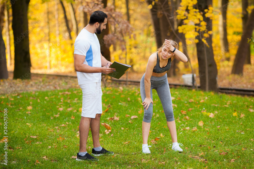 Fototapeta premium Fitness. Personal Trainer Takes Notes While Woman Exercising Outdoor