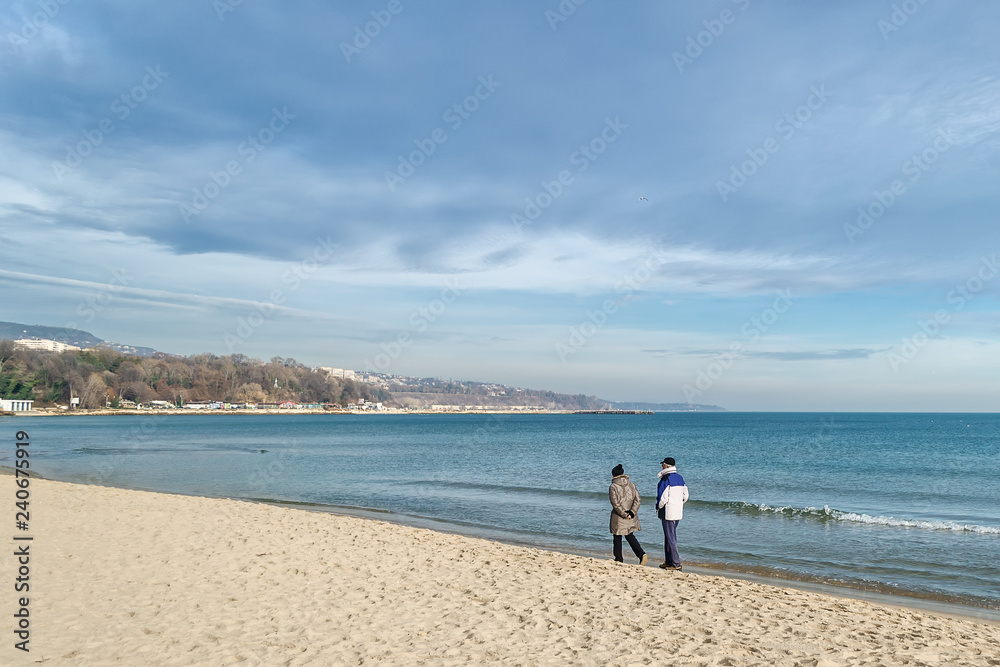 An elderly couple walking along the sea beach at the surf line on a warm sunny winter day An elderly couple walking along the sea beach at the surf line on a warm sunny winter day
