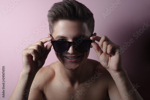 Close-up portrait of smiling teenage boy with sunglasses on pink studio background., with more shadows. © Lalandrew