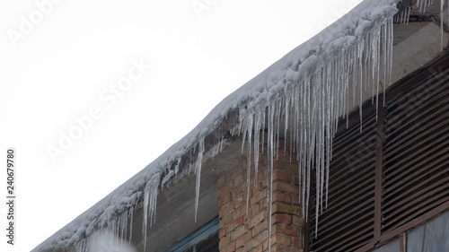 Icicles on the drainpipe and ditch. Incorrect installation of the drainage system, on which large icicles appear that pose a threat to the health and lives of people passing by. © maykal